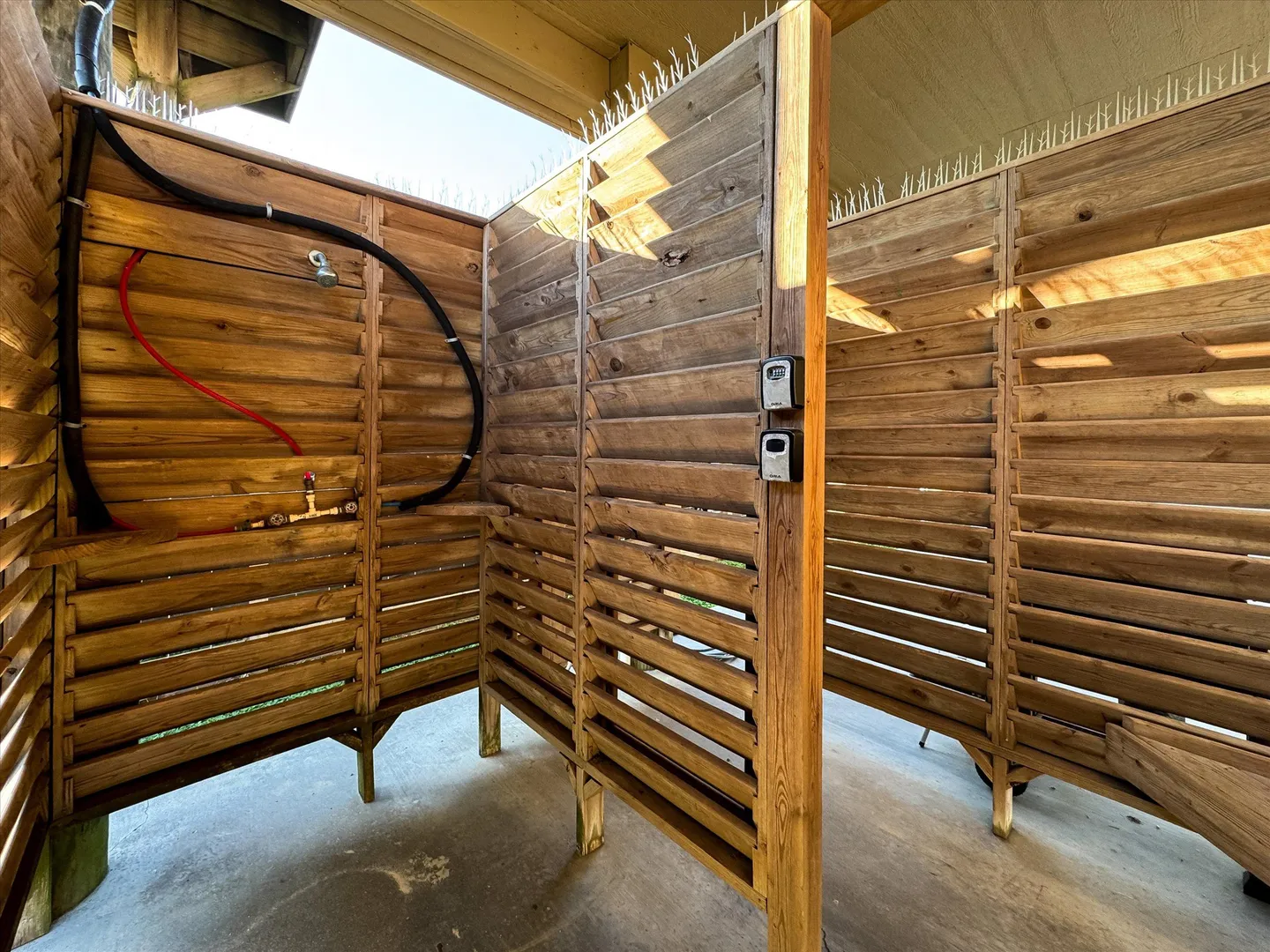 Outdoor shower stall enclosed by wooden louvered privacy walls on a concrete slab.