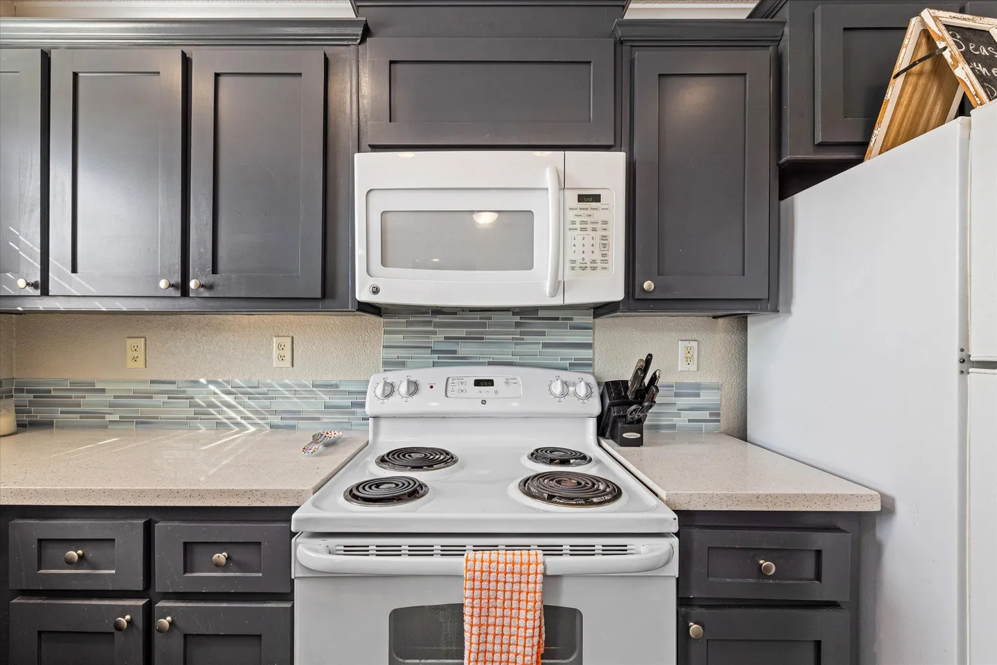 Kitchen cooking area with dark gray cabinets, an electric coil stove, an over-the-range white microwave, and light countertops.
