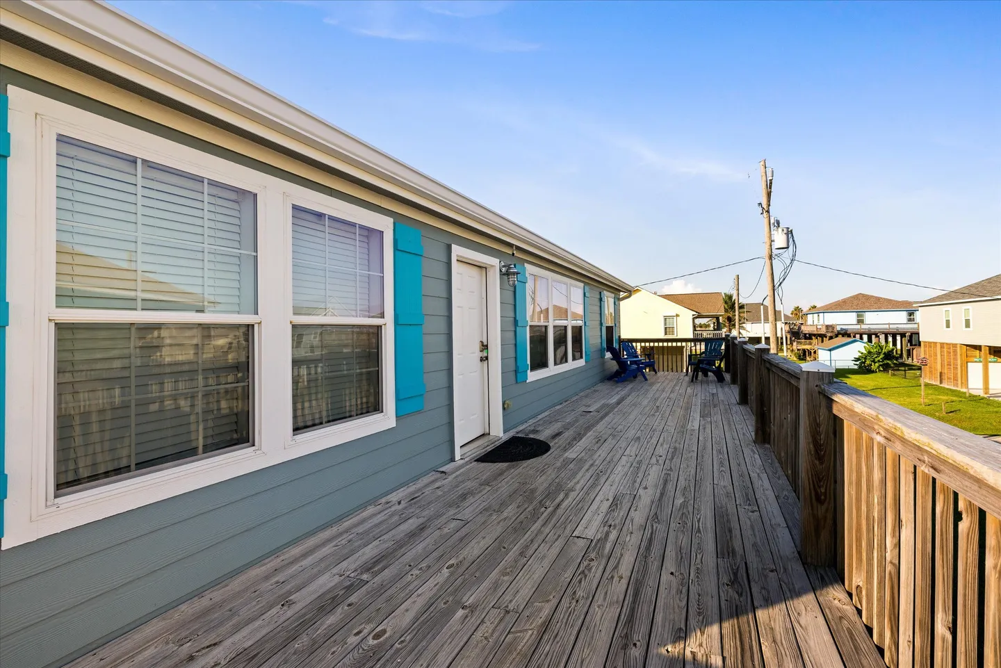 Exterior wooden deck running alongside a light blue house under a clear sky.