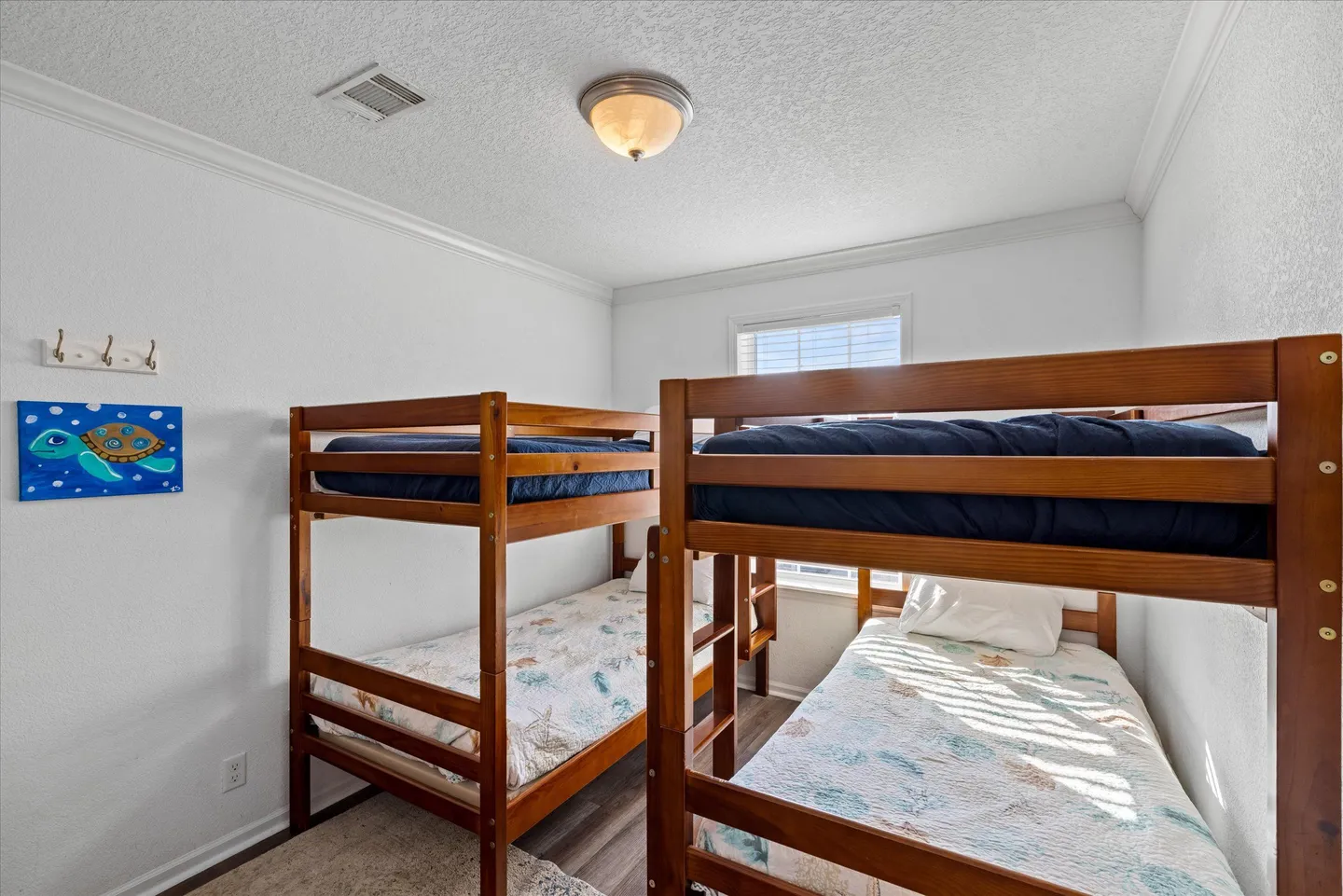 Bedroom featuring two wooden bunk beds with patterned quilts, white walls, and a window in the back.