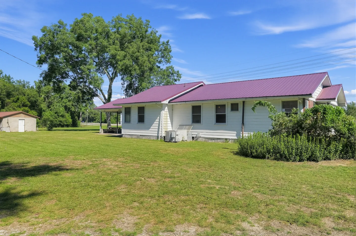 Exterior rear and side view of a single-story white home with a purple metal roof and large grassy lawn.