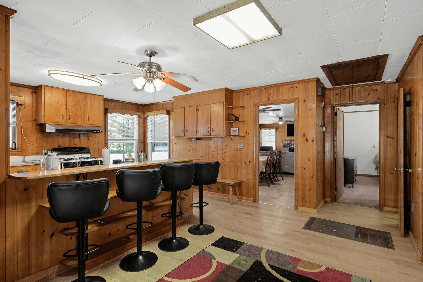 Kitchen and breakfast bar with wood-paneled walls, ceiling fan, and black barstools.