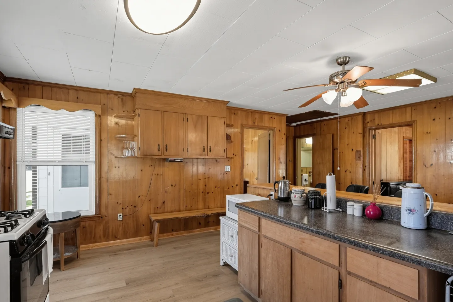 Kitchen interior featuring wood-paneled walls, matching wooden cabinetry, an island counter, ceiling fan, and light-toned flooring.