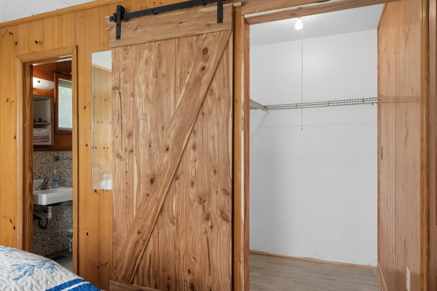 Wood-paneled bedroom showing a sliding barn door leading to an open closet and an open doorway to an en suite bathroom.