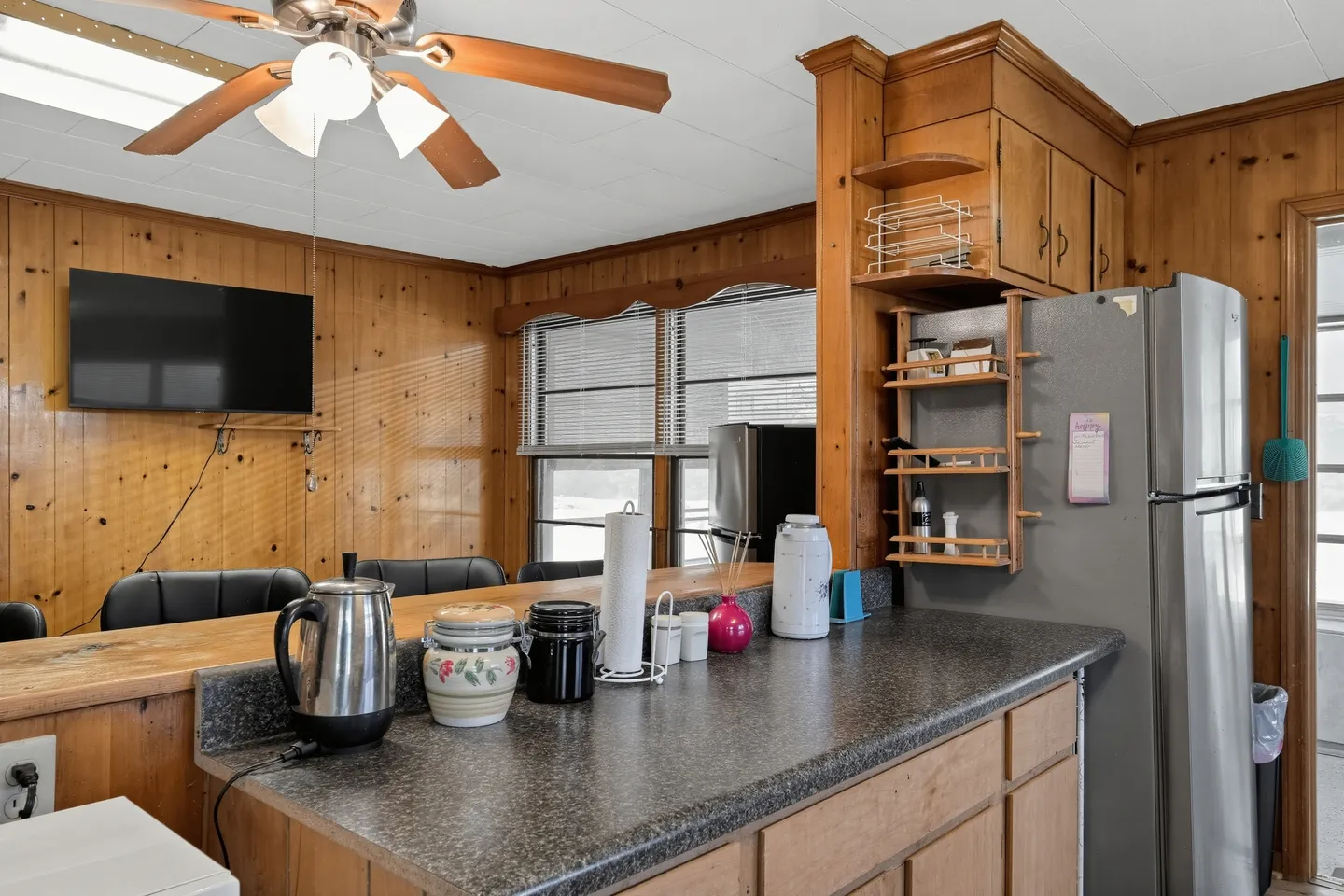 Kitchen counter overlooking a seating area with wood-paneled walls and a refrigerator.