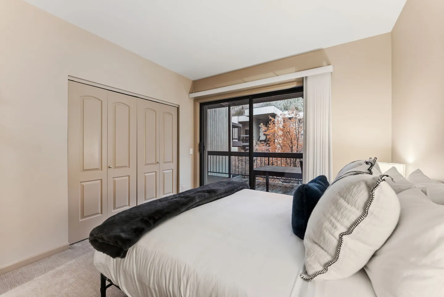 Bedroom with a made bed, carpeted floor, closet doors, and sliding glass door leading to a balcony.