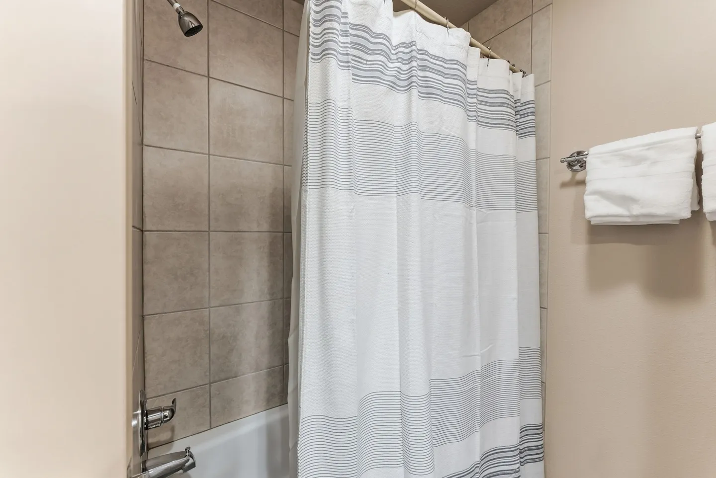 Bathroom shower and bathtub combo with tiled walls, striped shower curtain, and folded white towels on a wall rack.