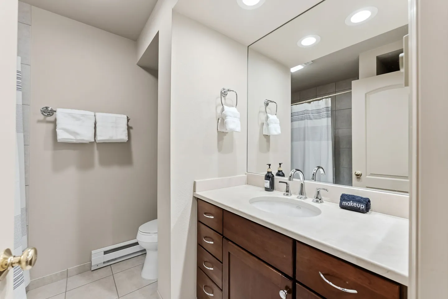Bathroom vanity with dark wood cabinets, a light countertop, a large mirror, and a glimpse of the toilet and shower.