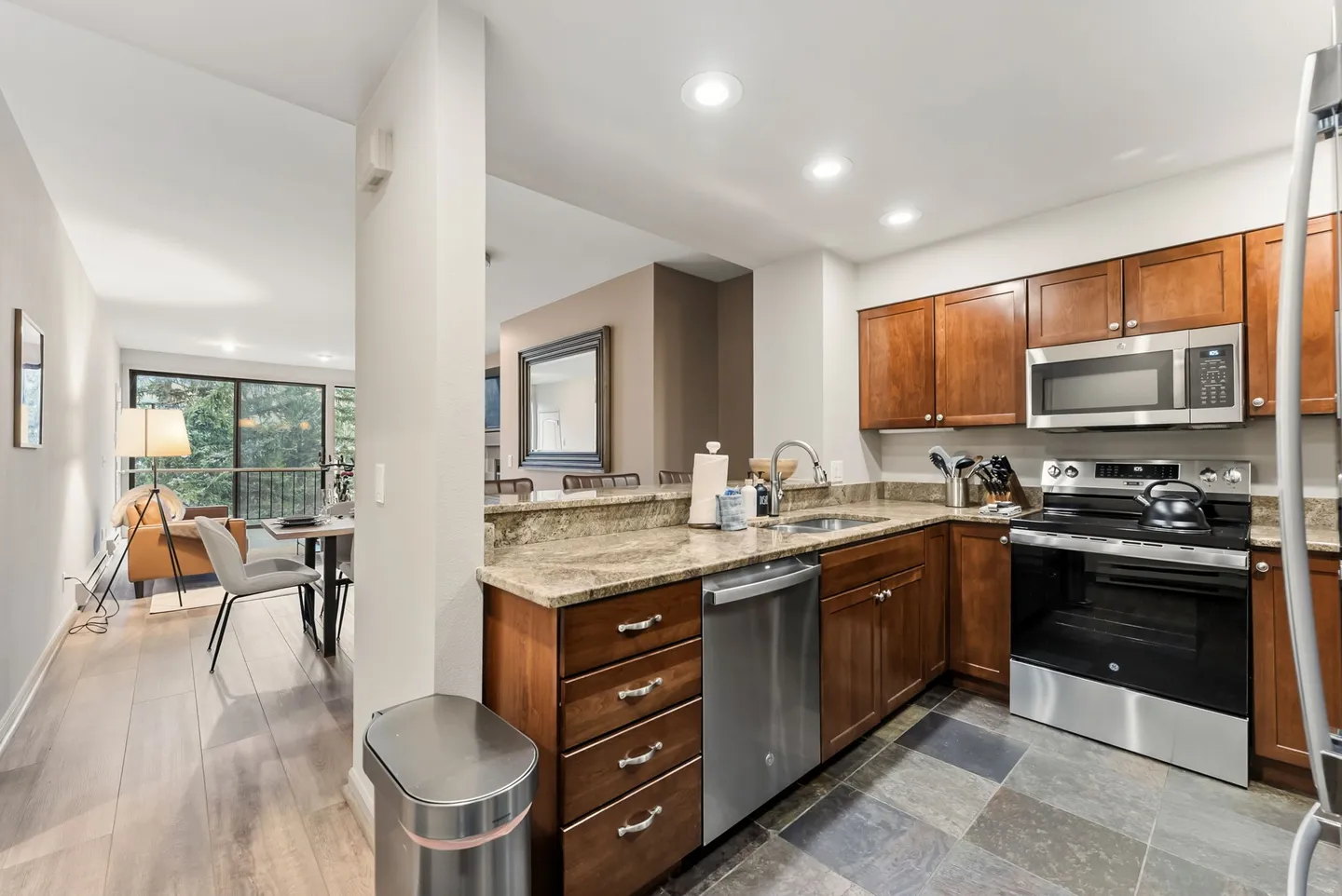 Kitchen with wooden cabinetry, stainless steel appliances, and view into the adjacent open living and dining area.