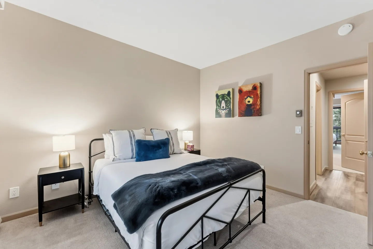 Bedroom with a black metal bed frame, neutral walls, two bear paintings, and carpeted floors.