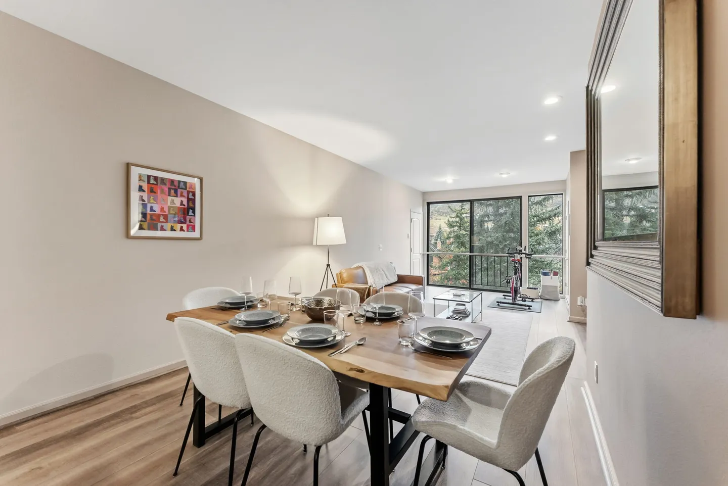 Dining area with a wood table and upholstered chairs leading into a living space with sliding glass doors.