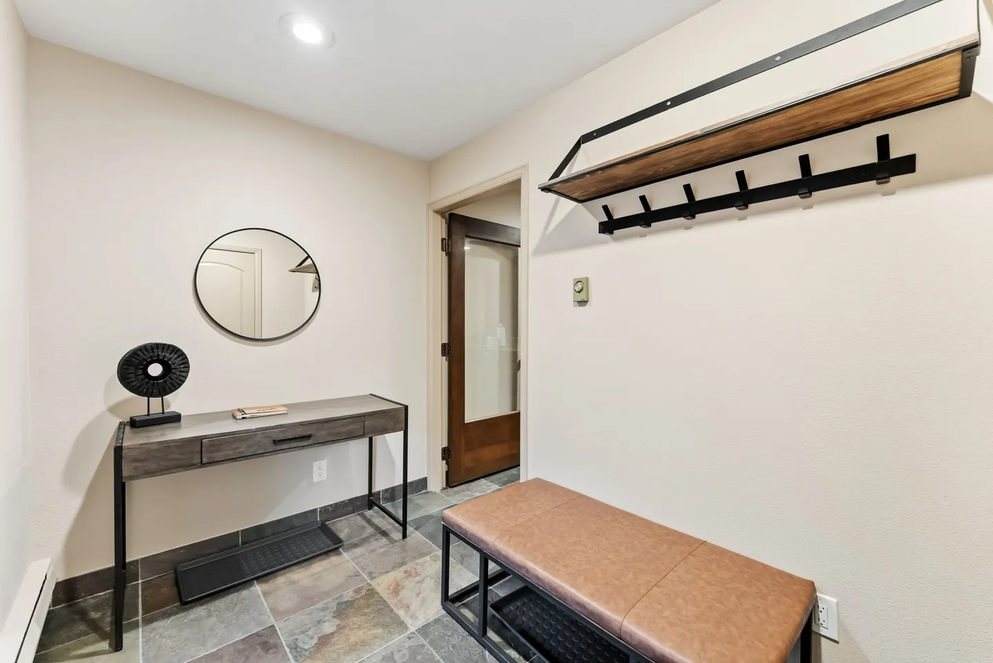Entryway with tile flooring, a brown bench, a console table with a round mirror, and a wall-mounted coat rack.