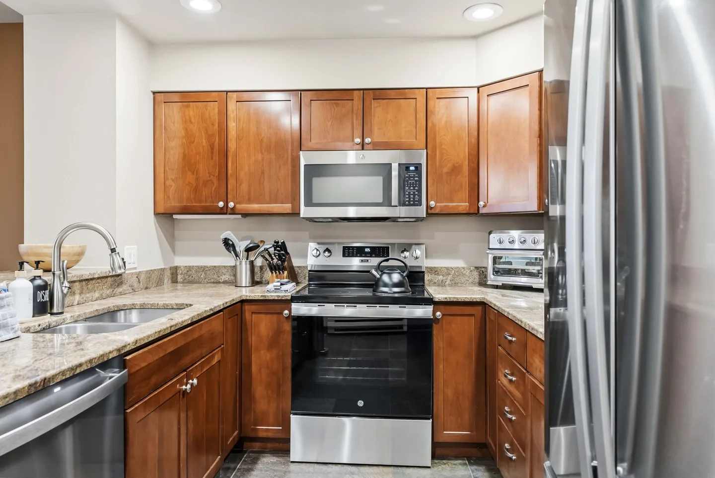Kitchen featuring warm wood cabinets, granite-look countertops, and stainless steel appliances including a range and microwave.