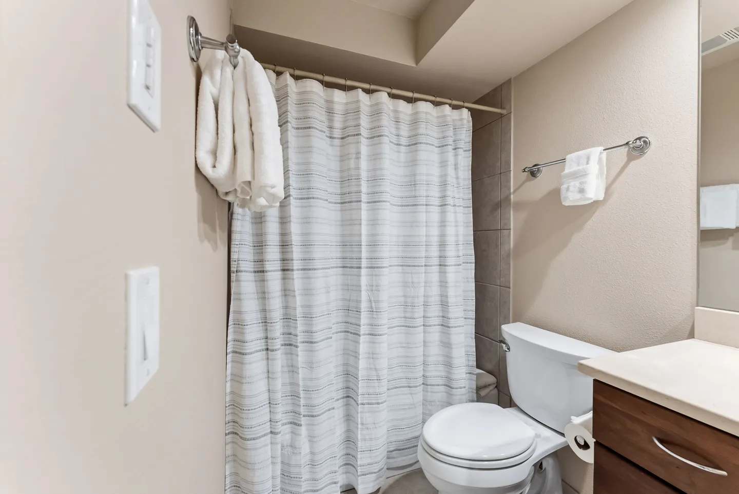 Bathroom showing a white toilet, a vanity counter, and a shower with a closed striped shower curtain.