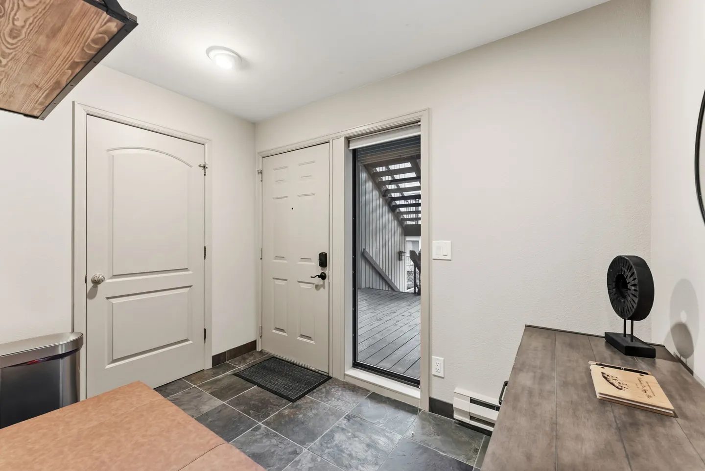 Entryway with dark tile flooring, a white front door, and a tall window looking out onto an exterior deck and staircase.