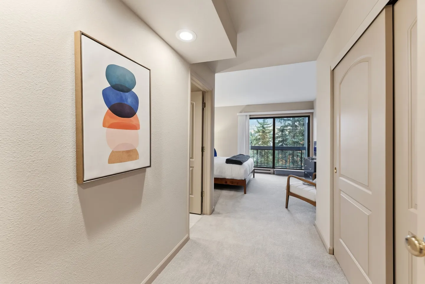 Hallway with abstract wall art leading toward a carpeted bedroom with a sliding glass door and balcony view.