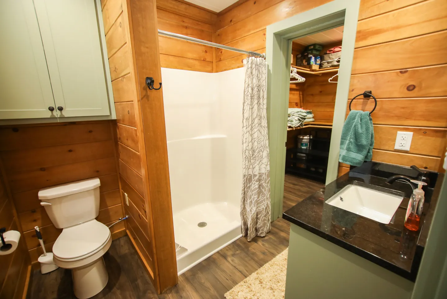 Bathroom with wood plank walls, toilet, walk-in shower stall, vanity with dark countertop, and doorway to a closet.
