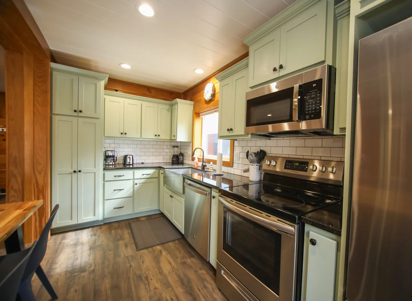 Kitchen featuring pale green cabinetry, stainless steel appliances, dark countertops, and wood-look flooring.