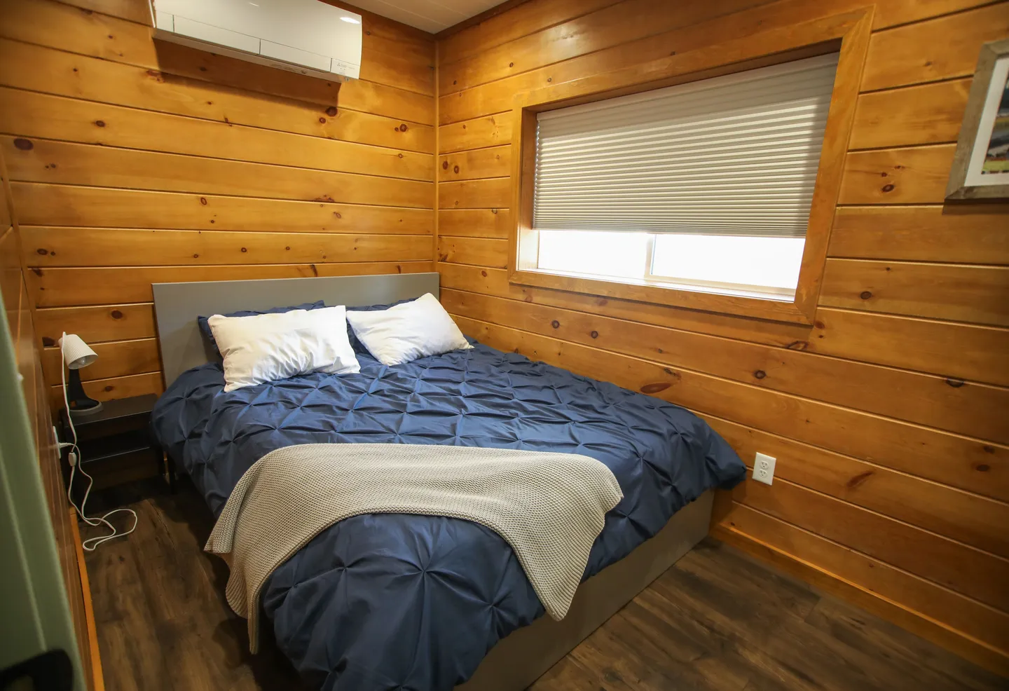 Bedroom with wood-paneled walls, a bed made with a dark blue comforter, and a window with blinds drawn.