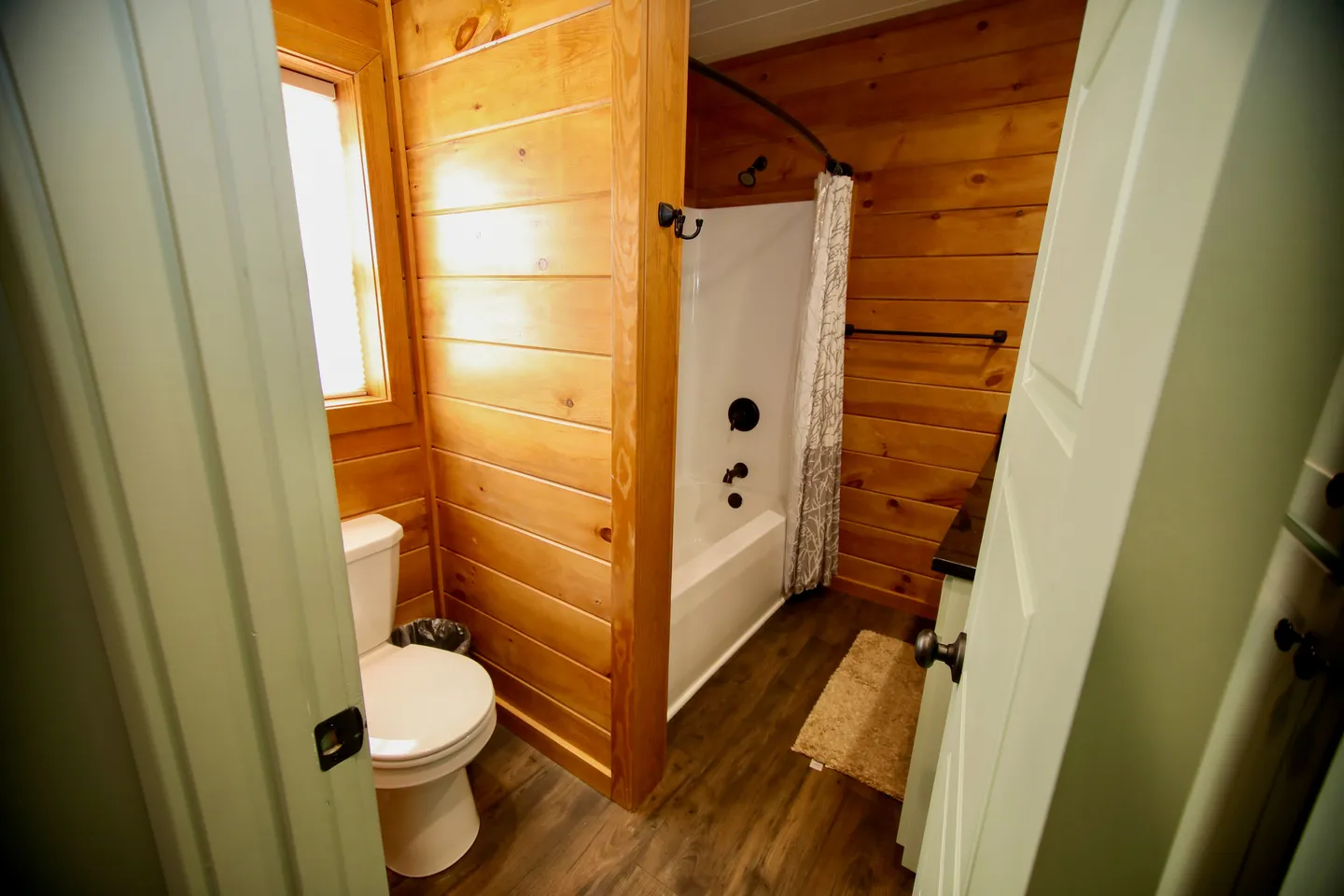 Bathroom with wood-paneled walls, a white toilet, and a white bathtub-shower combo framed by an open doorway.