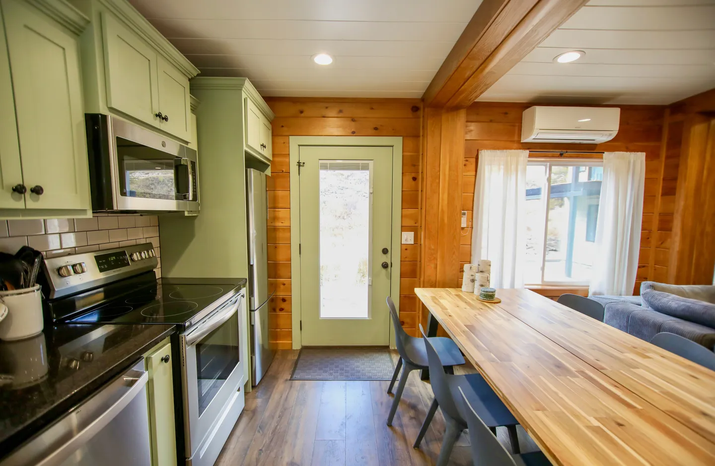 Kitchen and dining area featuring mint green cabinets, stainless steel appliances, a wooden dining table, and wood-paneled walls.
