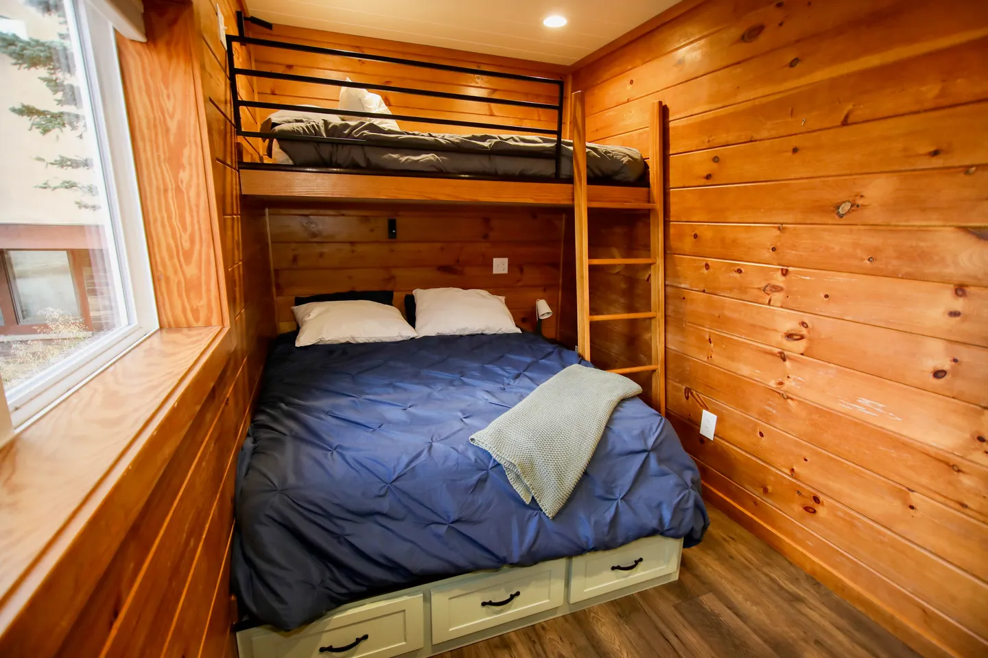 Wood-paneled bedroom alcove with a built-in bunk bed over a double bed and storage drawers underneath.