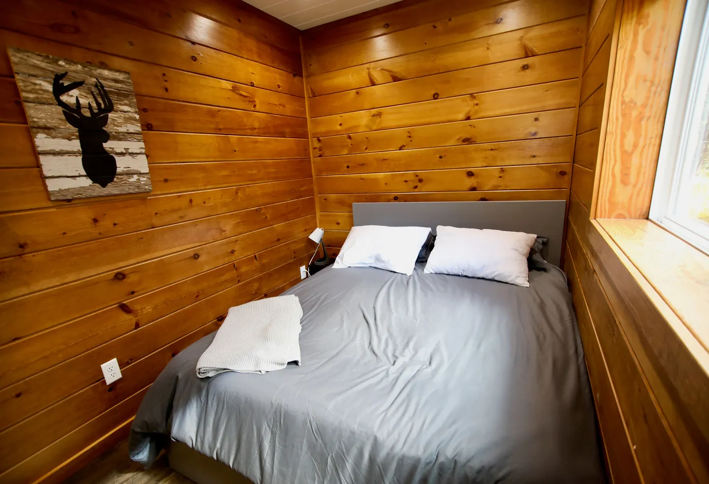 Bedroom with wood-paneled walls and a bed made with grey bedding and two white pillows.