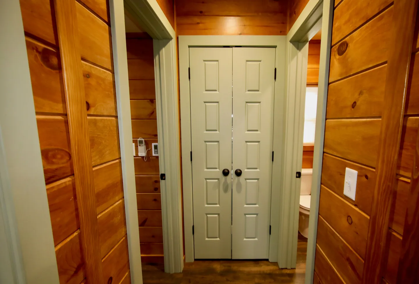 Hallway with wood-paneled walls, featuring closed double closet doors flanked by two doorways.
