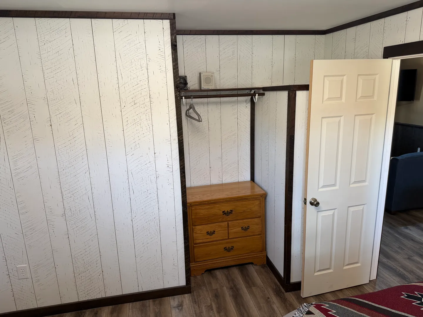 Open closet alcove in a bedroom with paneling, featuring a wooden dresser and hanging rod.