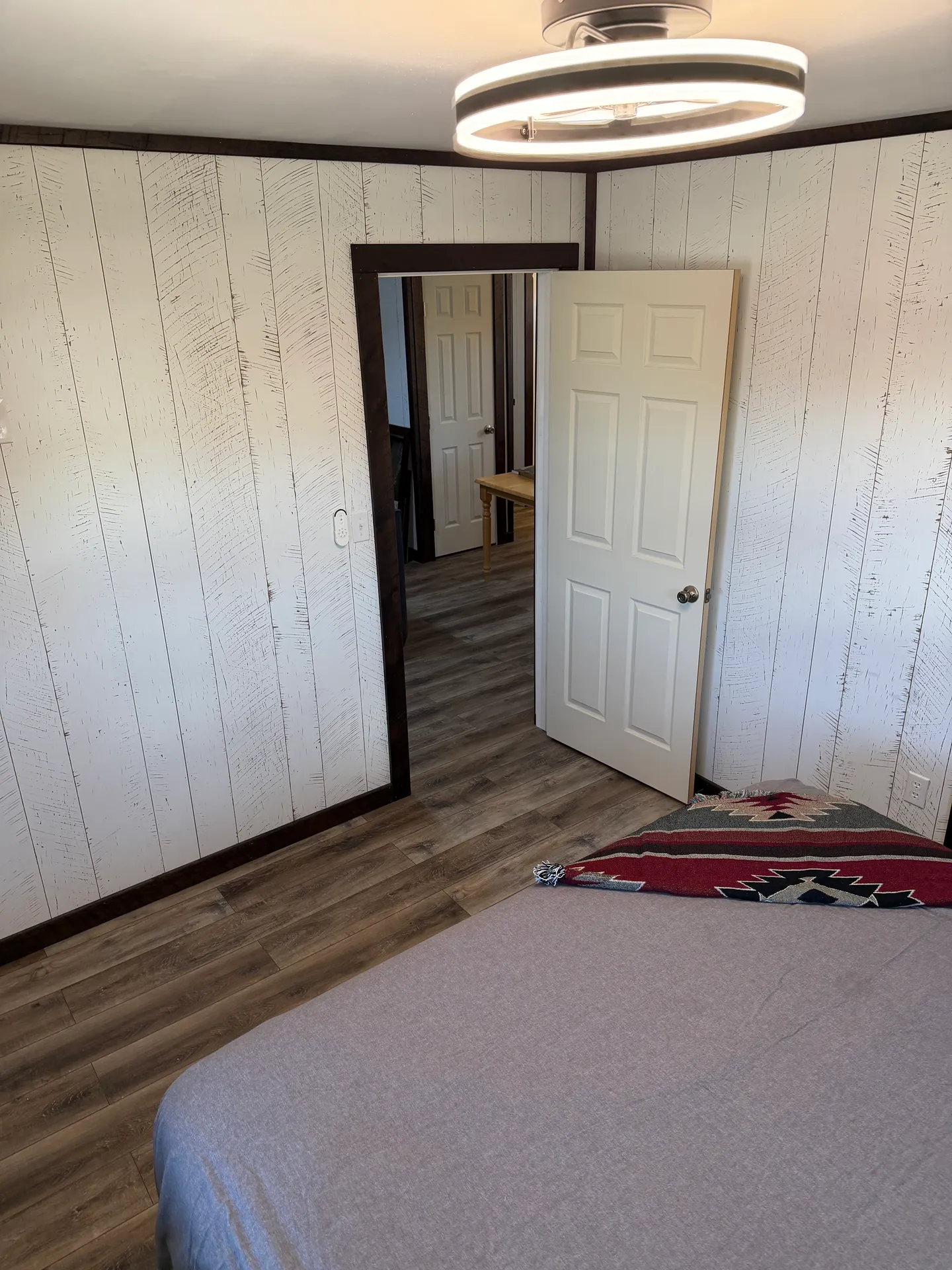 Bedroom with vertical panel walls, wood-look flooring, a circular ceiling light fixture, and an open doorway looking into a hallway.