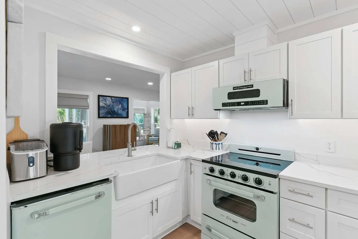 Kitchen featuring white shaker cabinets, pale green retro-style appliances, a farmhouse sink, and a passthrough window looking into a living room.