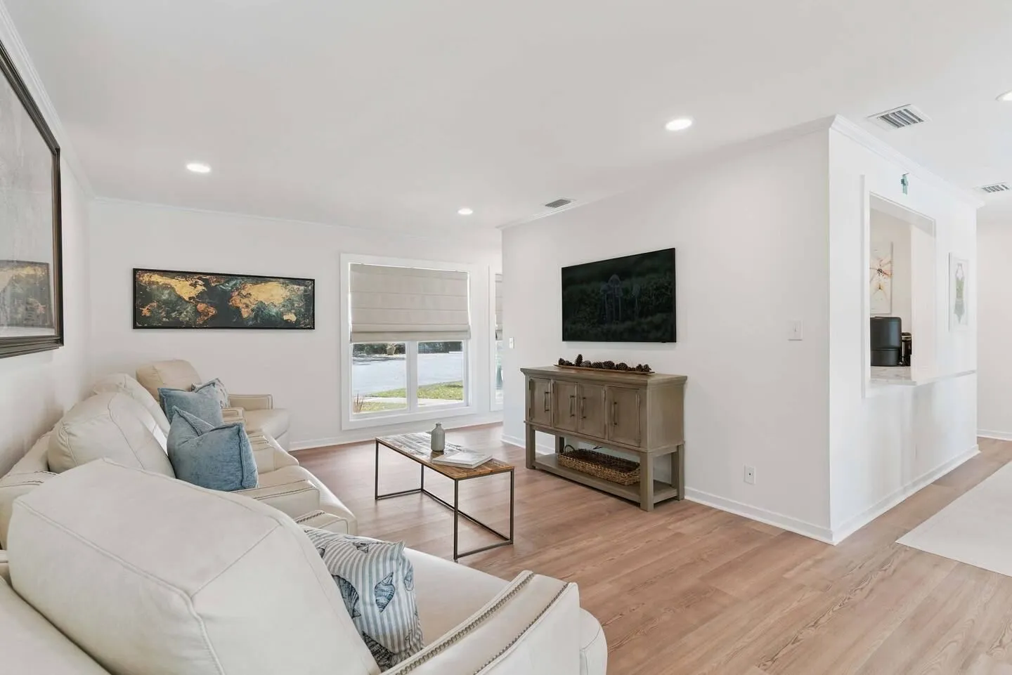 Bright living room featuring light wood-look flooring, a beige sectional sofa, a coffee table, and a wall-mounted TV above a console.