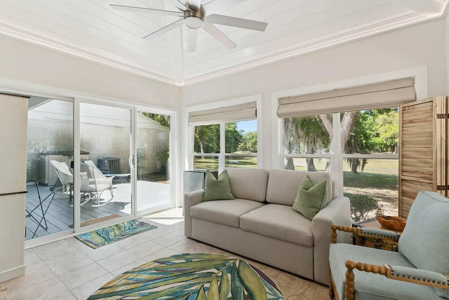 Sunroom with a sofa, armchair, sliding glass doors to a deck, and windows looking out to trees.
