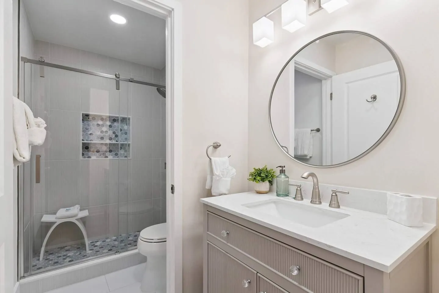 Bathroom featuring a vanity with a circular mirror, a toilet, and a glass-enclosed walk-in shower with tiled walls and a built-in niche.