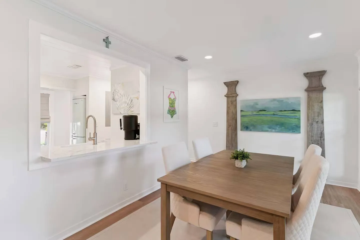 Dining area with a wooden table, upholstered chairs, and a pass-through window looking into the kitchen.