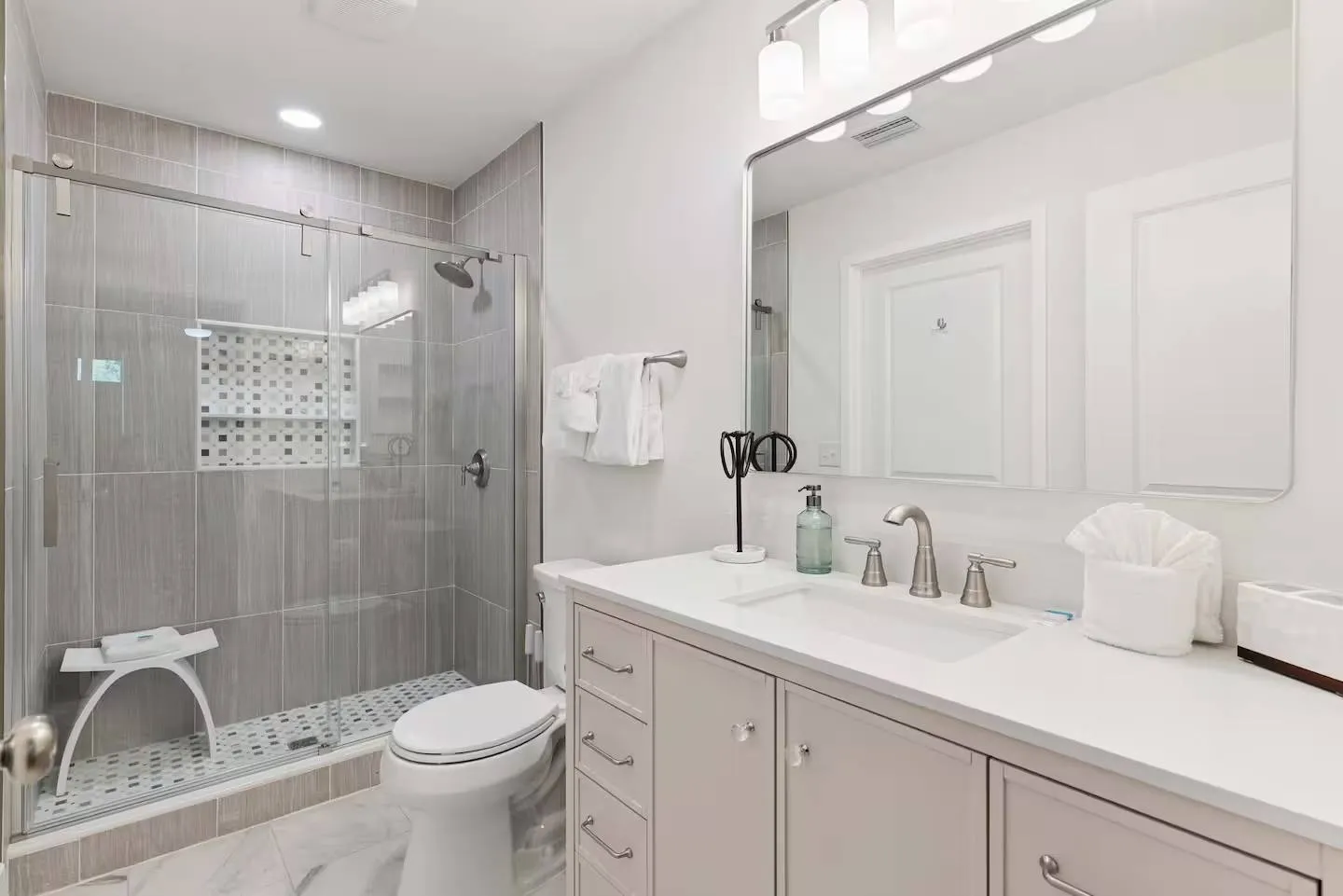 Bathroom featuring a vanity with a white countertop, large mirror, toilet, and a glass-enclosed walk-in shower with gray tile.