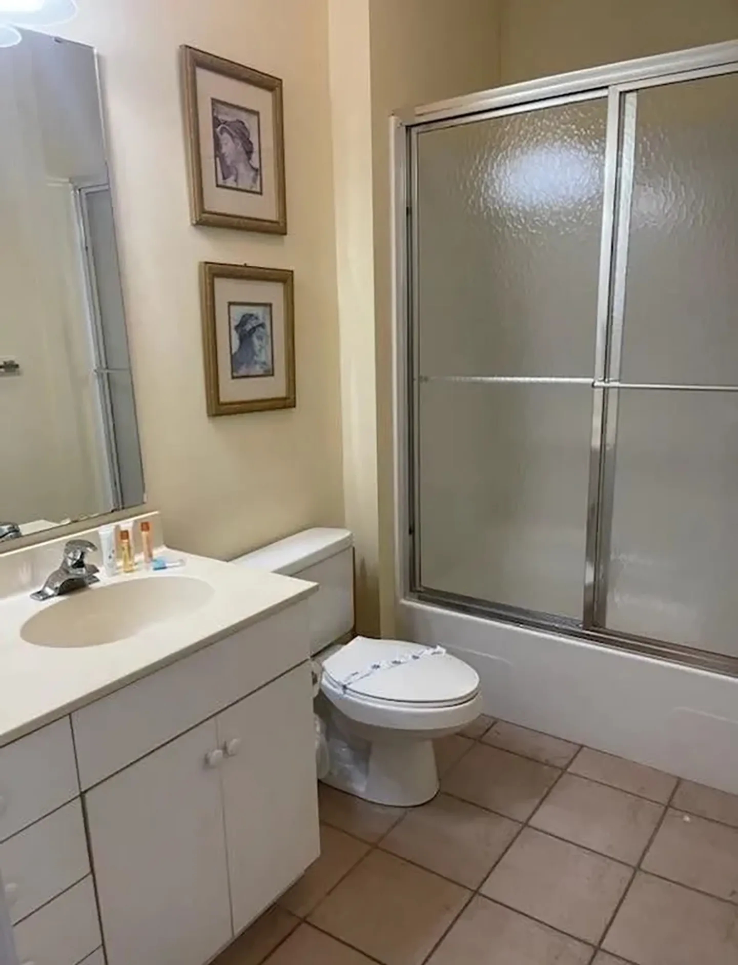 Bathroom with a white vanity, toilet, and a bathtub shower combo with sliding textured glass doors.