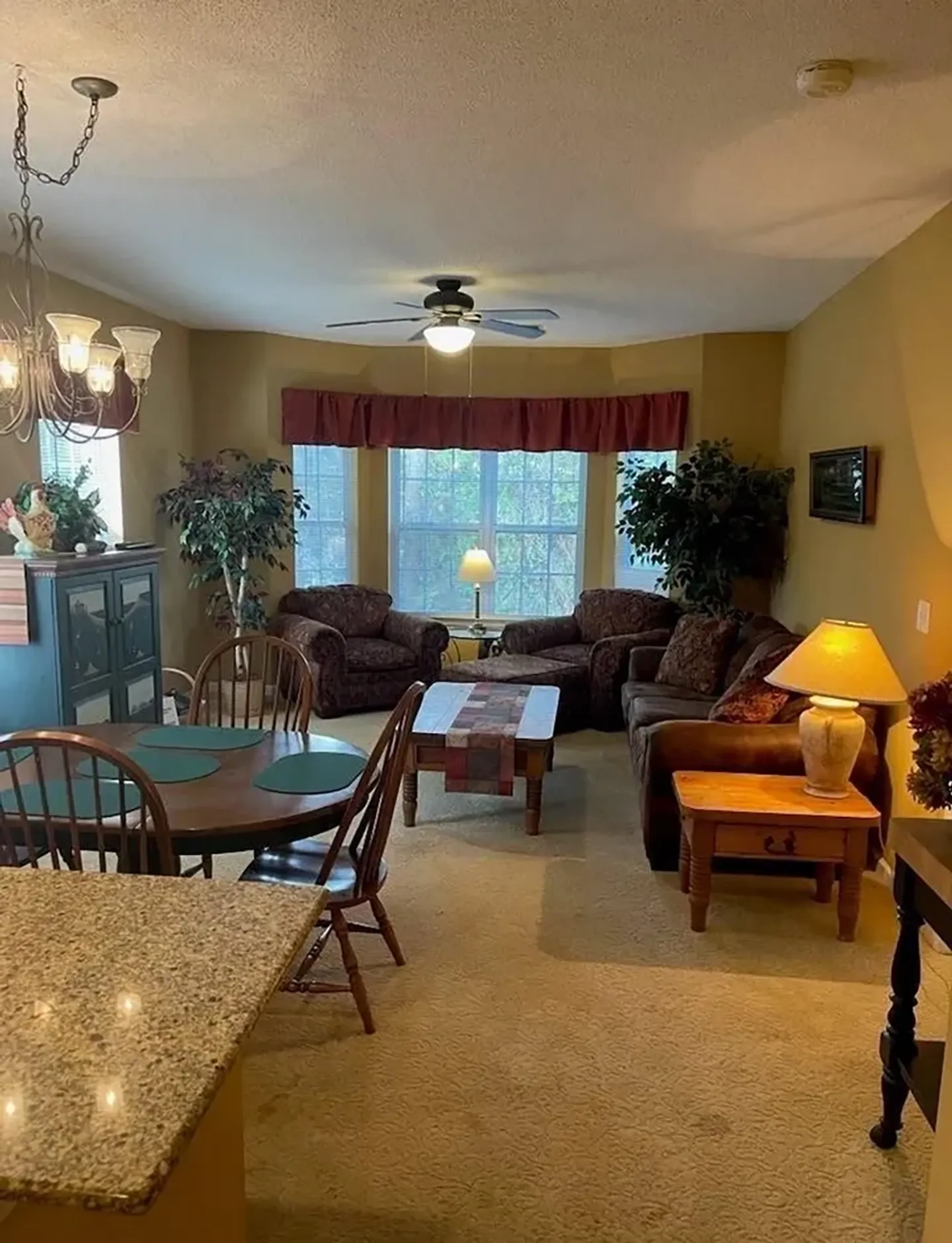 Open living and dining area featuring carpeted floors, a round dining table, and living room seating by a bay window.