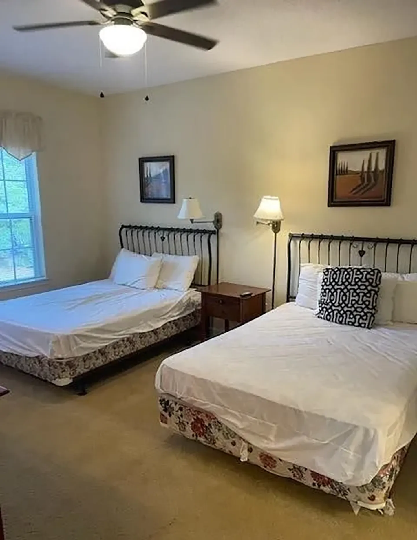 Bedroom with two beds featuring black wrought iron headboards, a bedside table, and carpeted flooring.