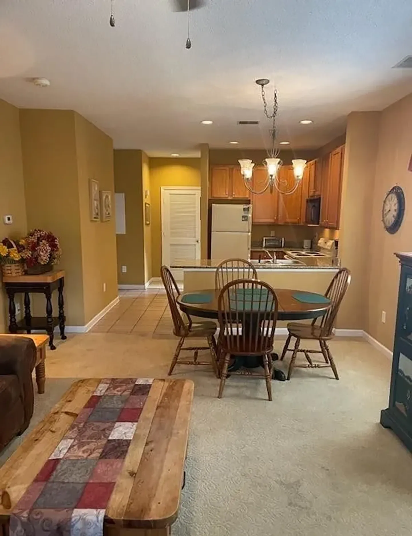Open-concept living and dining area with carpeted floors, a wooden dining set beneath a chandelier, and a view into the kitchen.