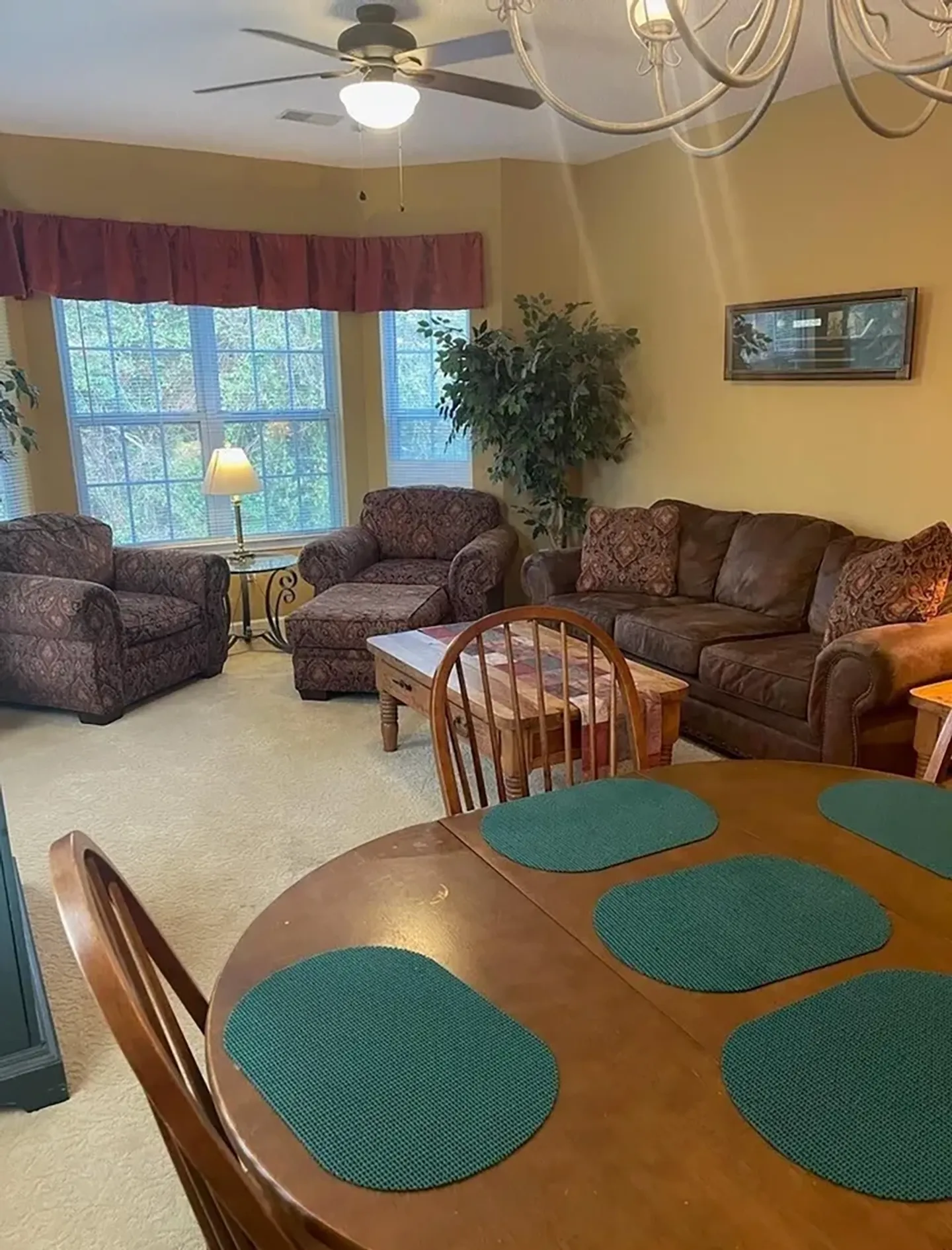 Living and dining area featuring a round wooden dining table in the foreground and a carpeted seating area with a sofa and armchairs.