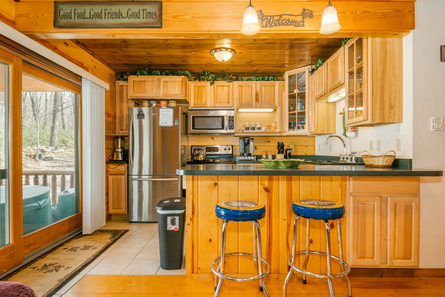 A kitchen with pine wood paneling, light wood cabinetry, stainless steel appliances, and a breakfast bar with two blue bar stools.
