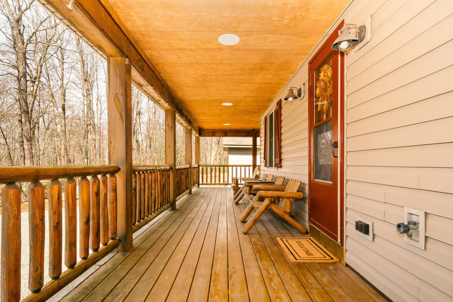 Covered wooden porch with rustic log railings, wooden deck flooring, and Adirondack chairs along the side of the house.