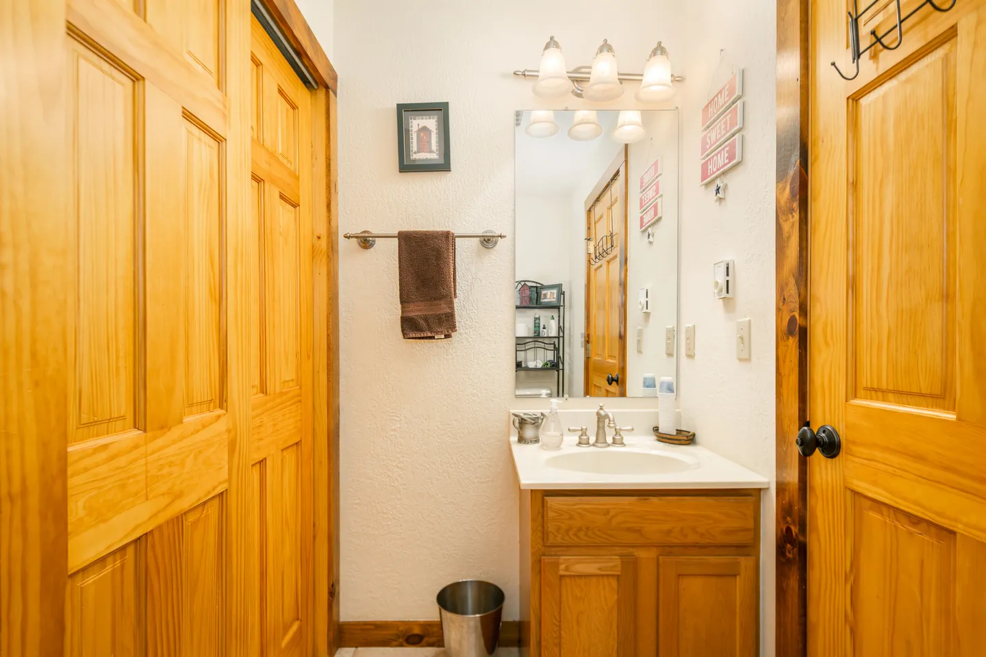Bathroom vanity with wooden cabinet, mirror, and light fixture flanked by wood paneled doors.