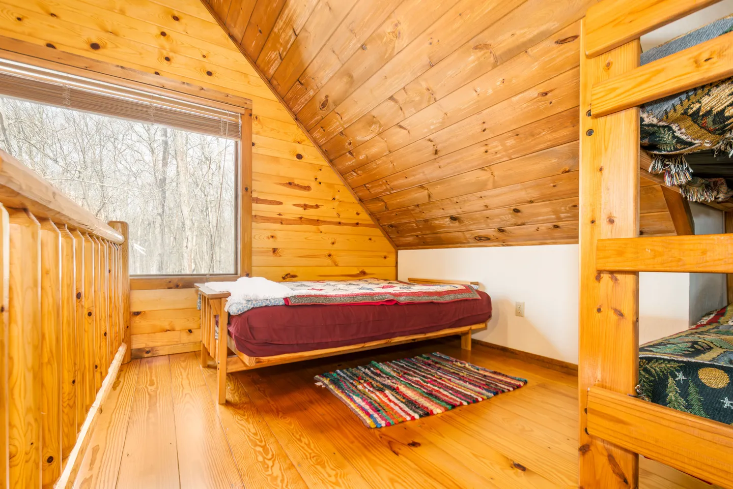 Upstairs loft with wood-paneled angled ceiling, twin-sized daybed, bunk beds, and wood flooring.