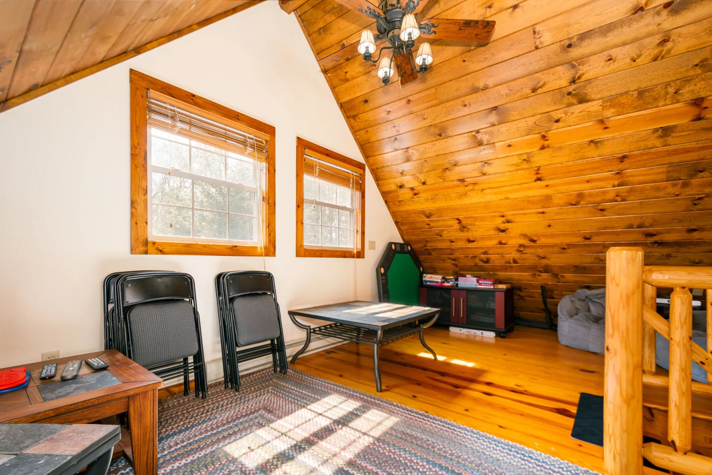 Upstairs loft area featuring wood-paneled angled ceilings, a low table, folded chairs, and games.
