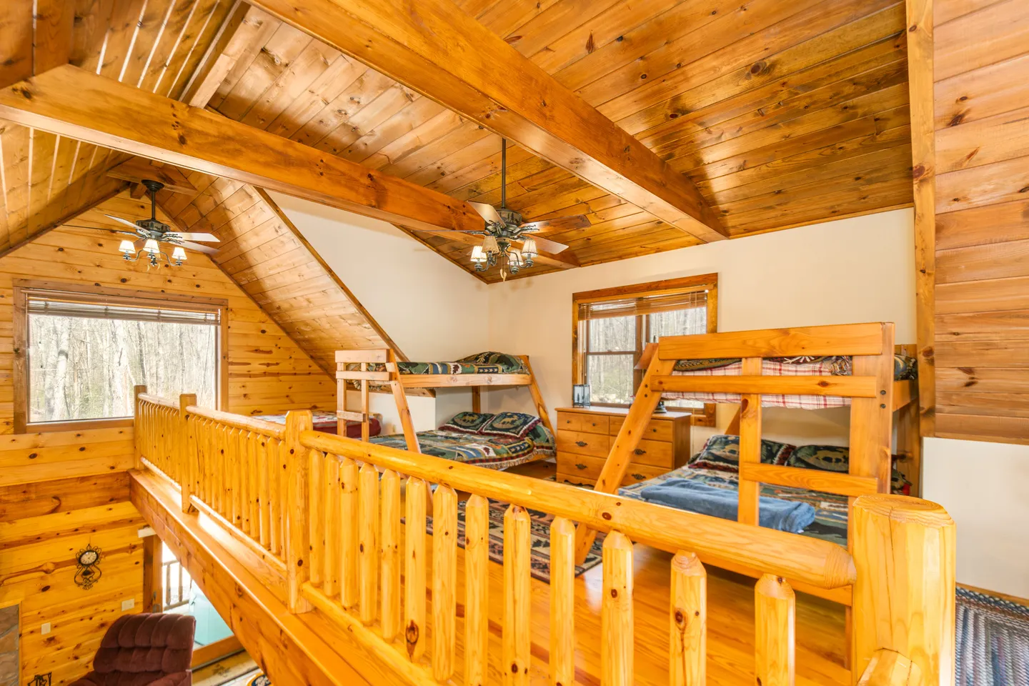 Loft bedroom area with wood-paneled vaulted ceiling, log railings, and two wooden bunk bed sets.