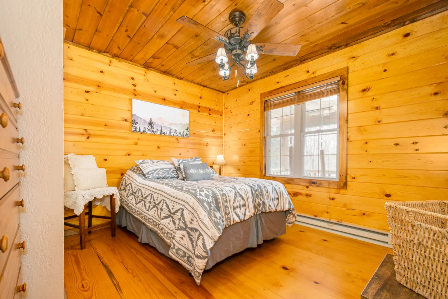 Bedroom with knotty pine wood-paneled walls, ceiling, and floor, featuring a bed with patterned bedding, a ceiling fan with lights, and a window.
