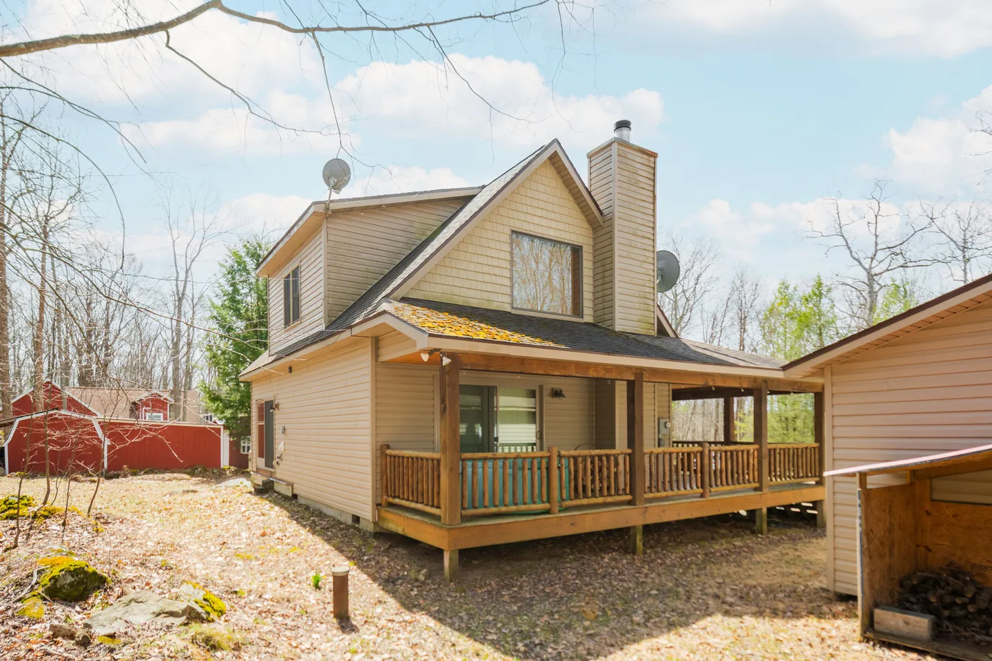 Exterior view of a multi-level tan house with a covered wooden porch, brick chimney, and surrounding yard with trees.
