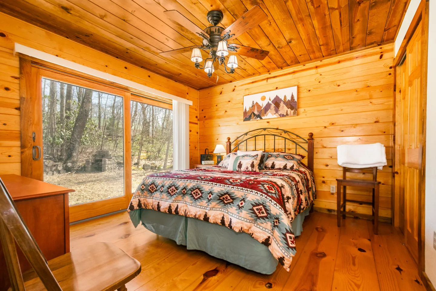 Bedroom with wood-paneled walls and ceiling, a bed with a southwestern-patterned quilt, and sliding glass doors to the outside.